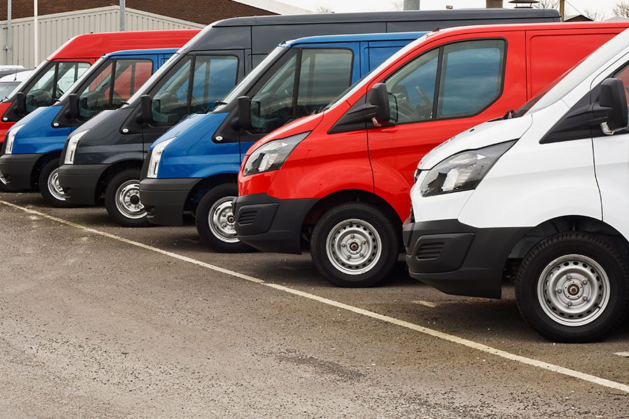 Business Insurance - A Fleet of Red, Blue, Black, and White Transportation Vans Parked in a Row at a Parking Lot During the Daytime